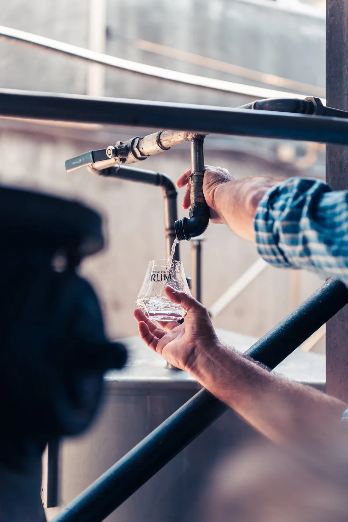 Hände, die Rum aus einem Hahn in ein Verkostungsglas füllen